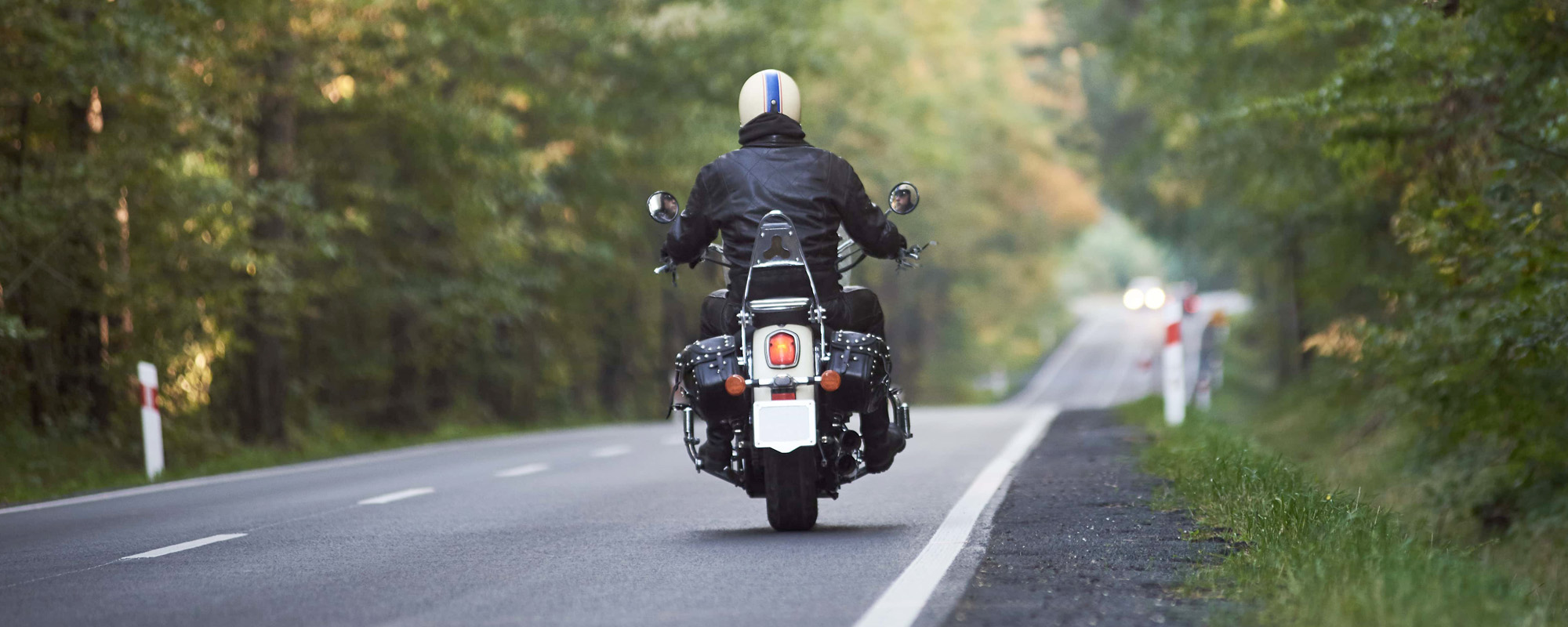 Biker in black leather outfit driving modern powerful motorcycle along sunny road on summer day