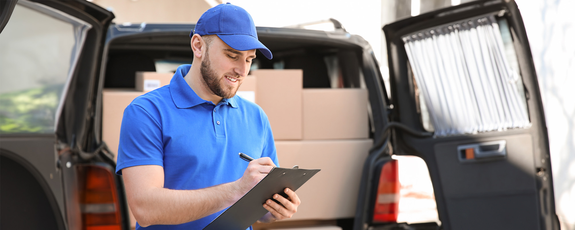 Handsome delivery man with clipboard near car outdoors