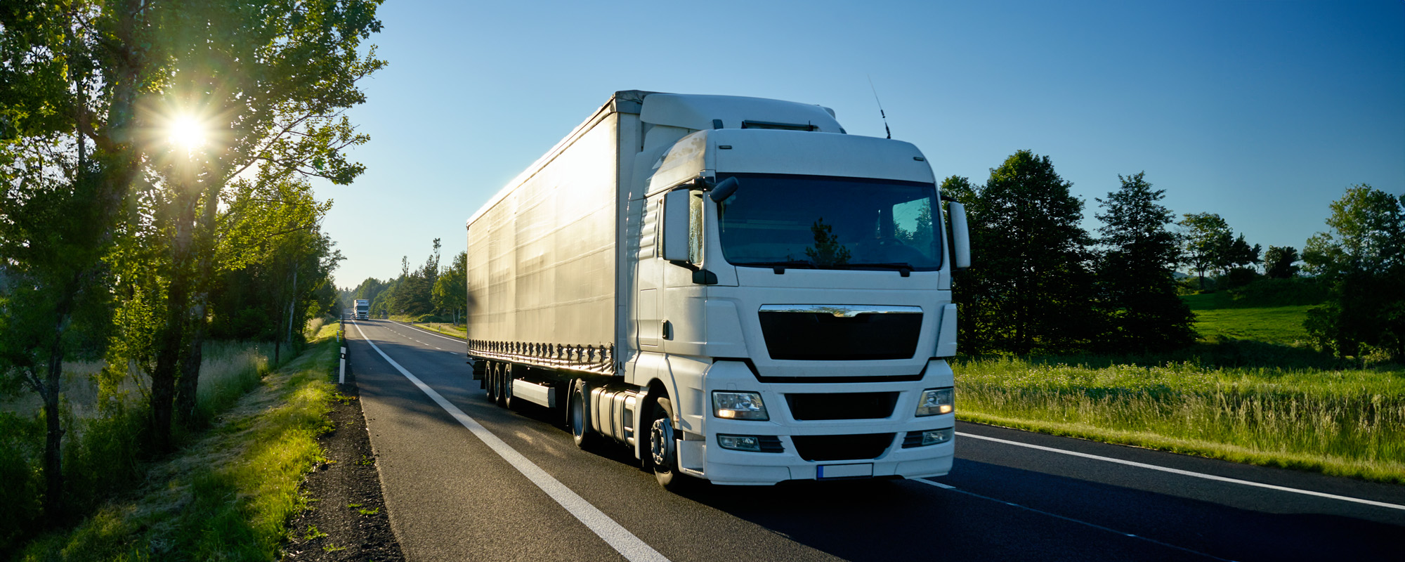 White truck driving on the road lined with deciduous trees with a star shining rays of the sun