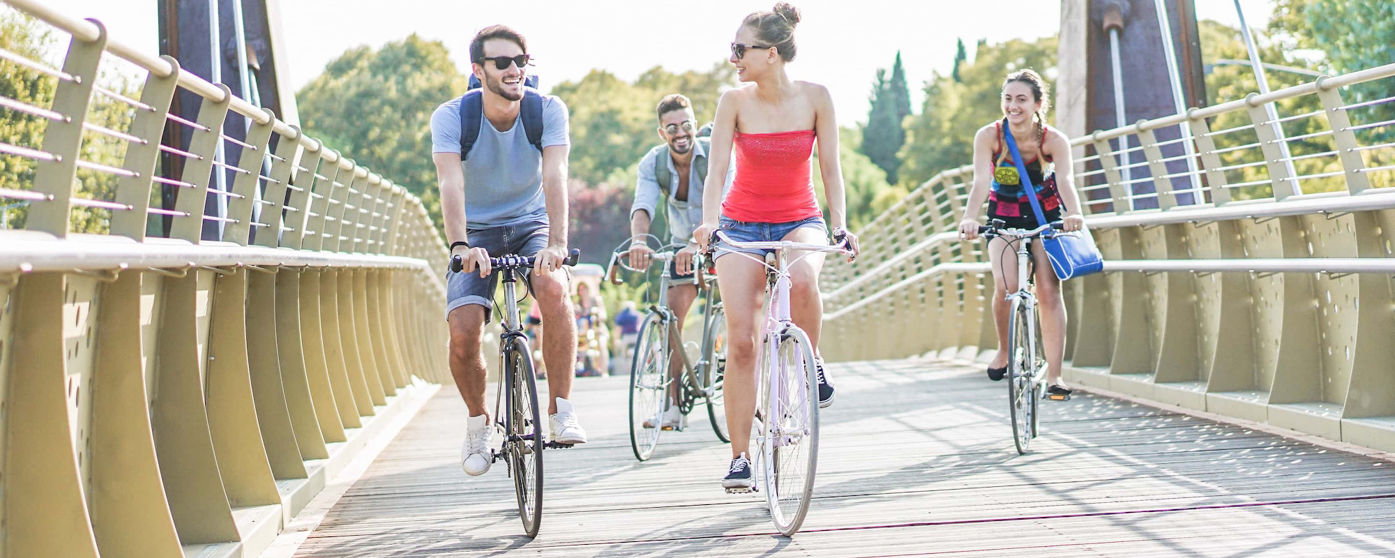 happy friends running bicycles on bridge city park